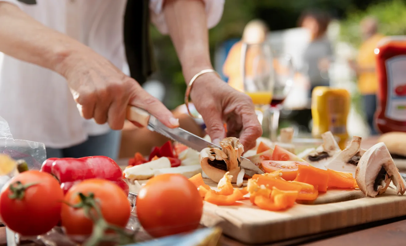 mani di donna che tagliano funghi e altre verdure per preparare spiedini nel contesto di una sagra tradizionale