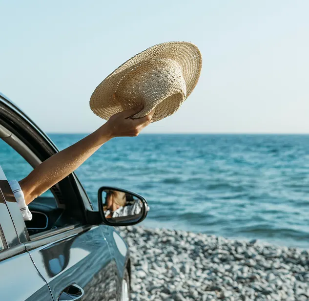arm out of the window of a car parked on a beach in corsica, holding a summer hat